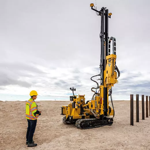 Operador a utilizar o sistema de controlo e orientação Trimble Groundworks 3D num estaleiro de construção com um bate estacas amarelo em funcionamento, demonstrando precisão e eficiência no trabalho