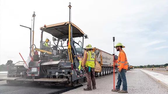 Trabajadores con chalecos reflectantes operando una extendedora de asfalto guiada con sistema 3D Trimble Roadworks