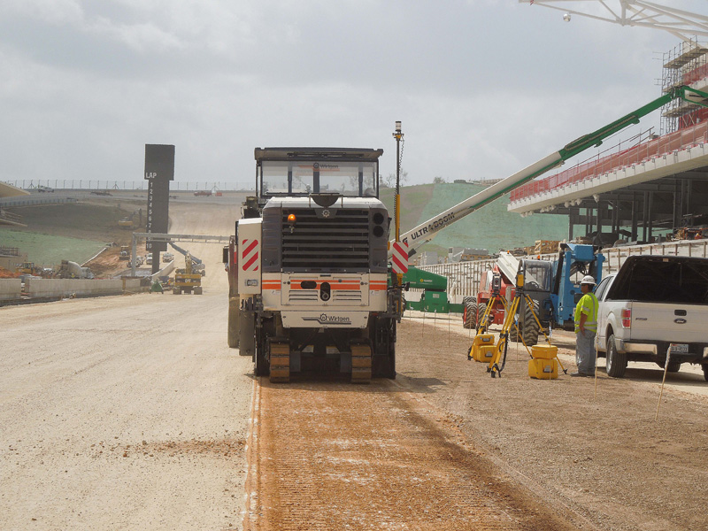 Máquina pavimentadora de asfalto Dynapac a trabalhar num estaleiro de construção com vários equipamentos e trabalhadores ativos – ilustrando os sistemas de orientação para pavimentadoras e fresadoras SITECH