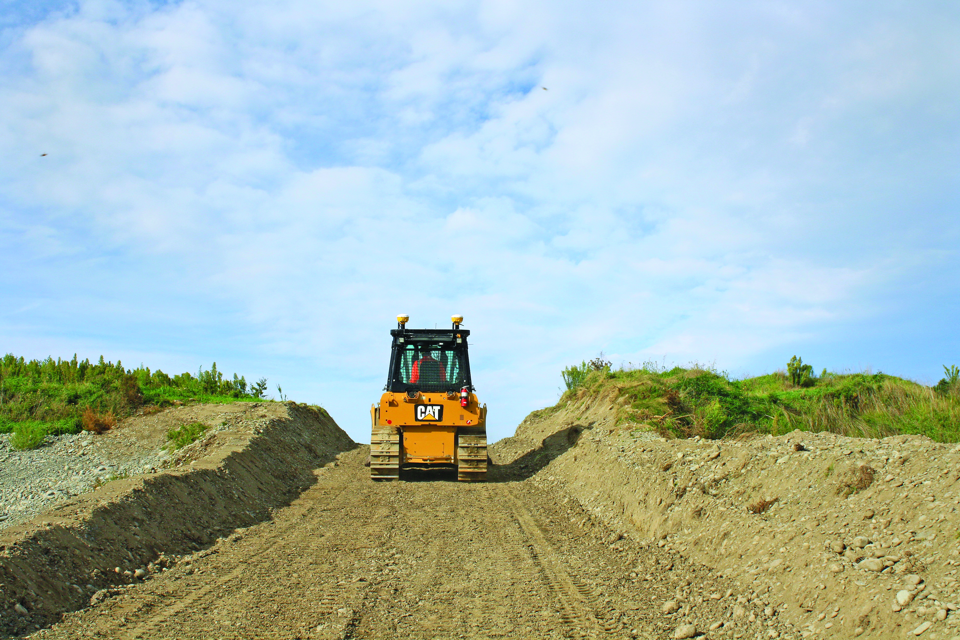 Un bulldozer CAT amarillo equipado con el sistema 3D Trimble Earthworks trabaja en un terreno de construcción con montículos de tierra a ambos lados