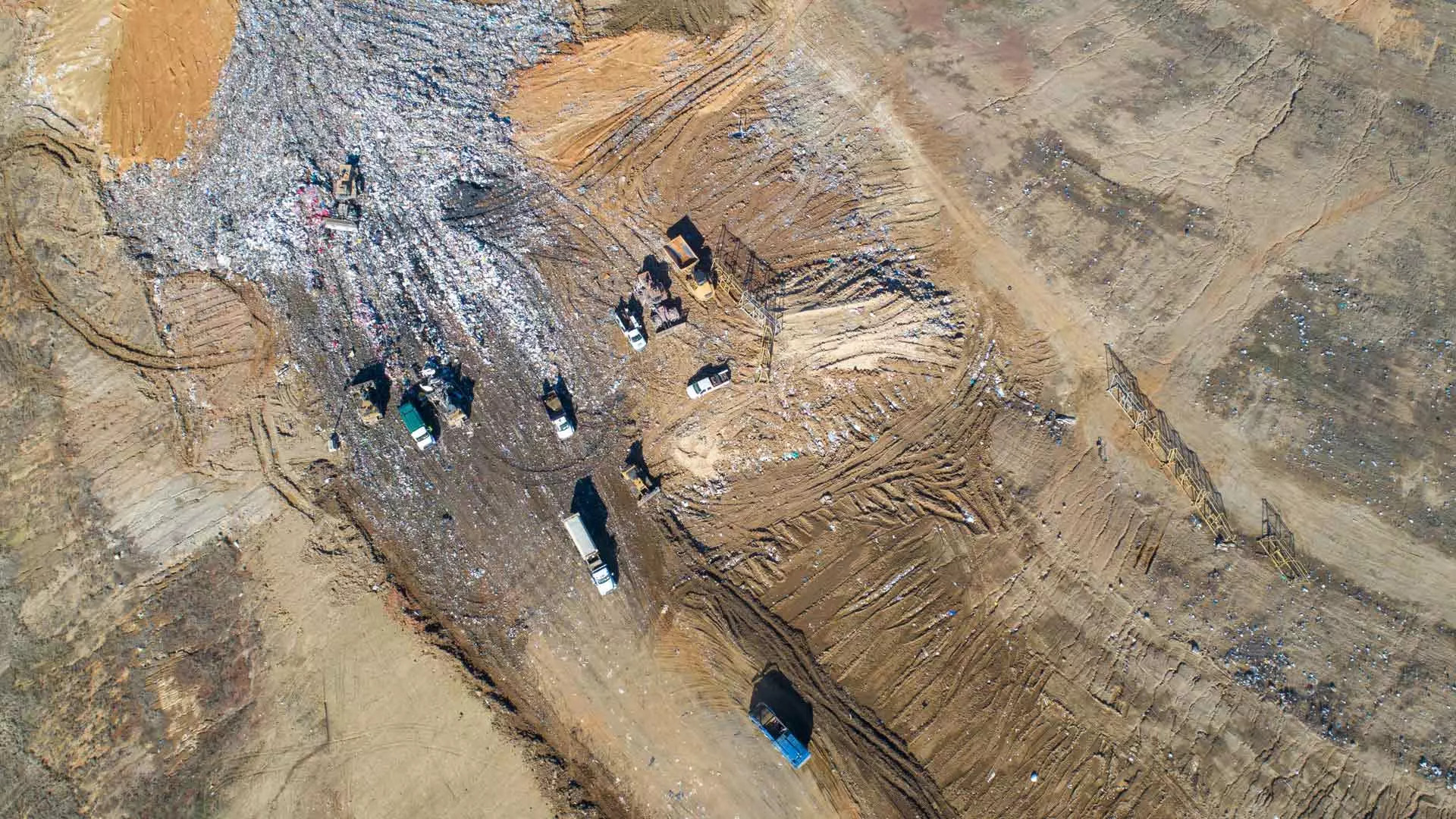 Vista aérea de um aterro sanitário em funcionamento com máquinas pesadas e gestão de resíduos em curso. A imagem mostra a extensão da área, com diferentes secções para resíduos, solo e materiais recicláveis, destacando a importância das soluções eficientes de gestão de aterros da Trimble distribuídas pela SITECH.